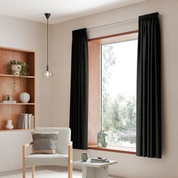 Curtains and blinds Black curtains framing a window with a view of greenery, in a room with a wood shelving unit, books, and a white armchair with a grey cushion.