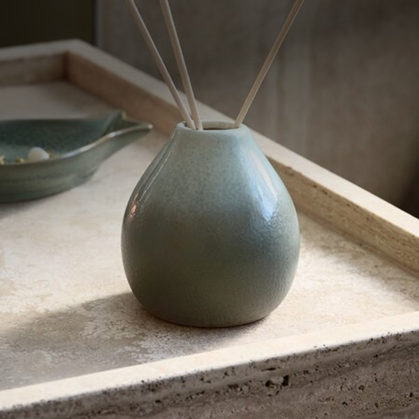 Reed diffusers Teal ceramic reed diffuser with wooden reed sticks, on a stone tray beside a small dish.