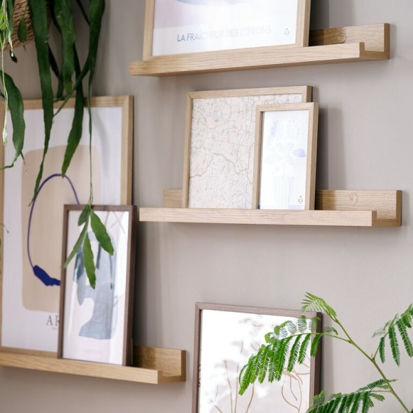Shelves Oak picture ledge shelves mounted at staggered heights, displaying framed art prints and trailing potted plants.