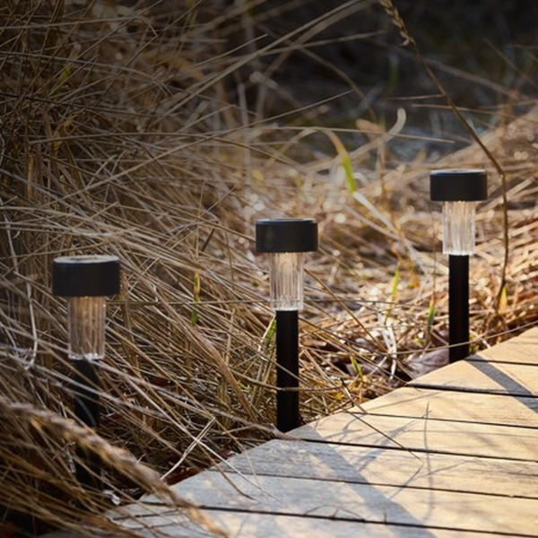 Solar lights Three black solar garden path lights with clear ribbed stems, staked along a wooden boardwalk edge among tall grasses.