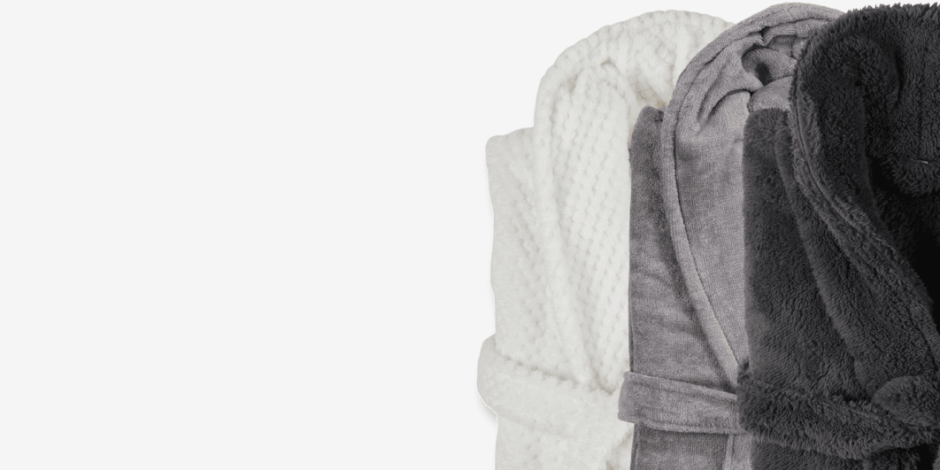 Bathrobes Three rolled bathrobes in white, grey, and charcoal plush fabric, shown against a plain light background.