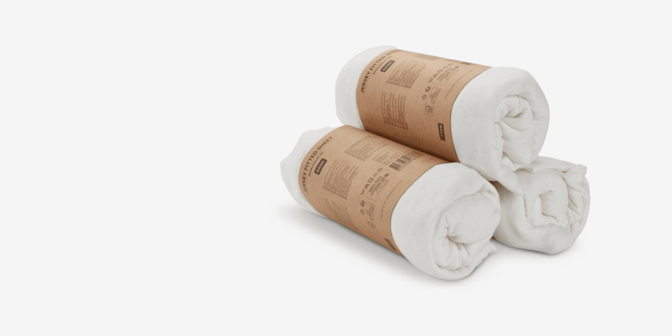 Sheets Two rolled white jersey fitted sheets wrapped in kraft paper packaging bands, shown against a plain light grey background.