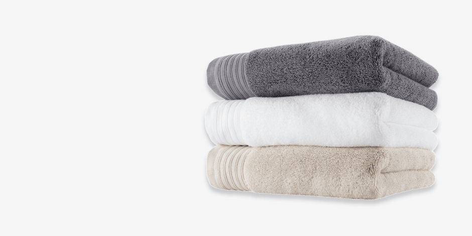 Towels Stack of folded bath towels in grey, white, and beige, shown against a plain light background.