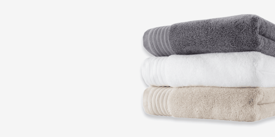 Towels Stack of folded bath towels in grey, white, and beige, shown against a plain light background.